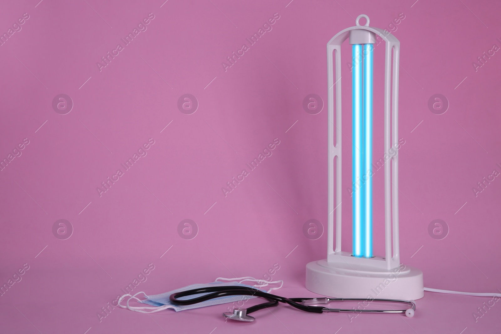 Photo of Ultraviolet lamp, medical masks and stethoscope on pink background, space for text