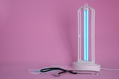 Ultraviolet lamp, medical masks and stethoscope on pink background, space for text