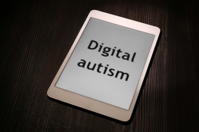 Photo of Tablet with phrase Digital Autism on wooden table. Addictive behavior