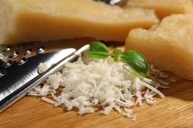 Photo of Grated parmesan cheese with basil near grater on wooden table, closeup