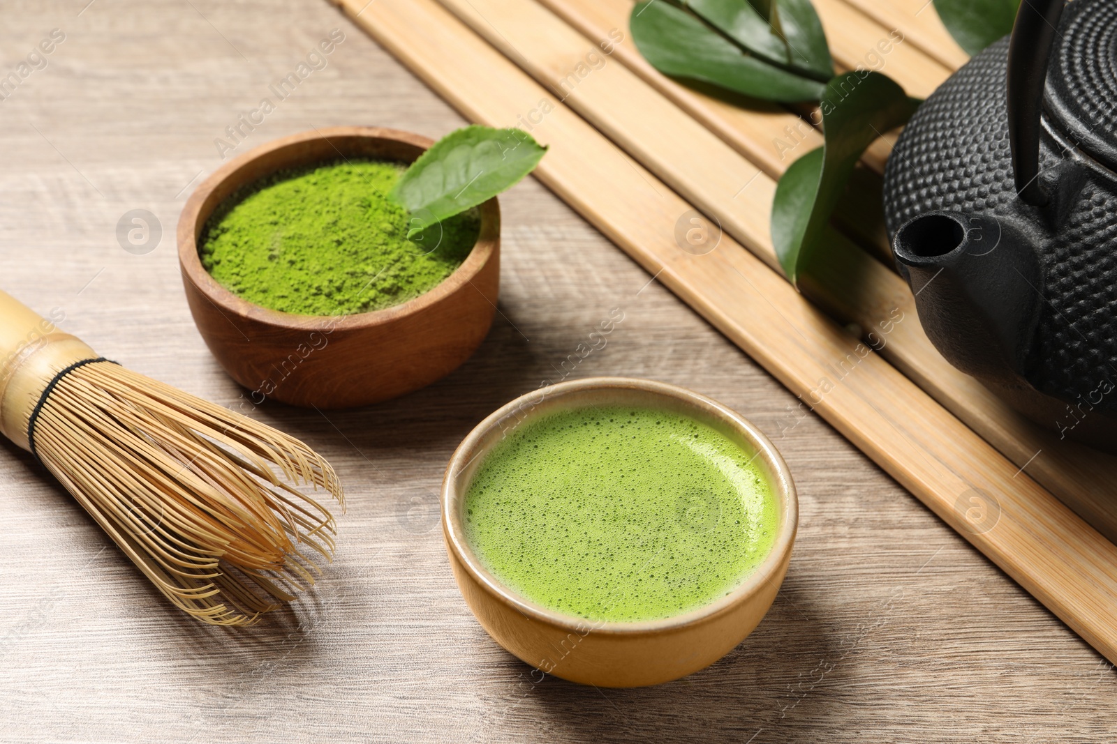 Photo of Cup of fresh matcha tea, bamboo whisk, teapot and green powder on wooden table