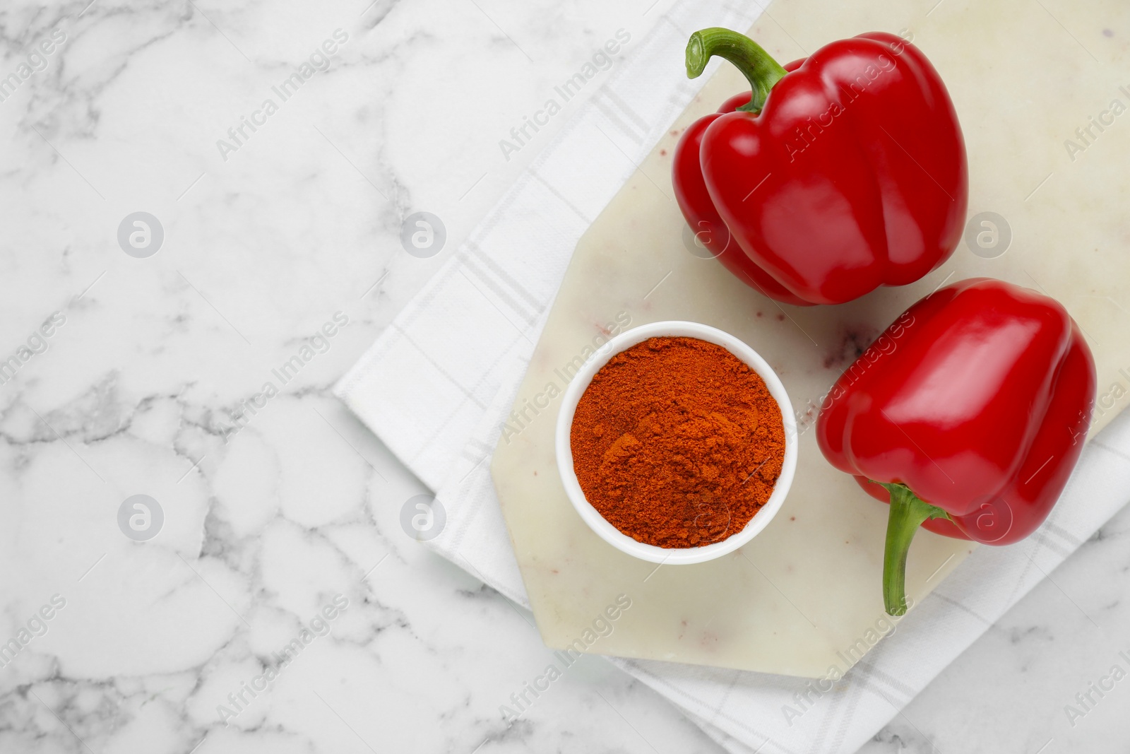 Photo of Bowl with aromatic paprika powder and fresh bell peppers on white marble table, flat lay. Space for text