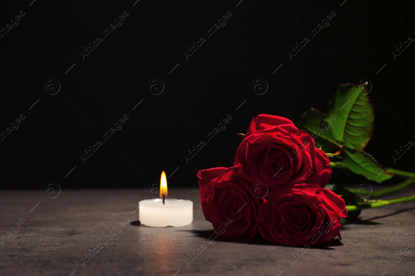 Photo of Beautiful red roses and candle on table against black background. Funeral symbol
