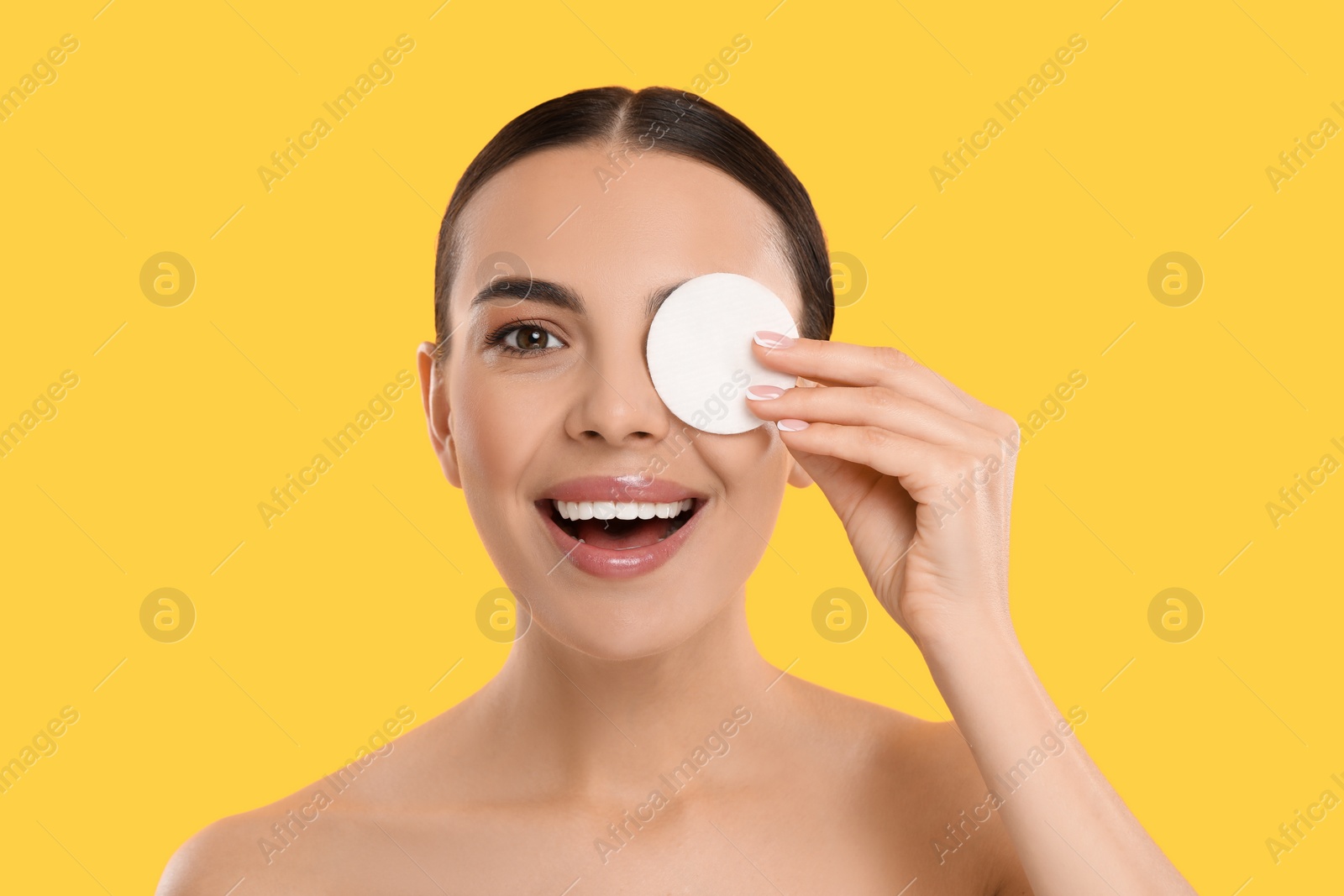 Photo of Beautiful woman removing makeup with cotton pad on yellow background