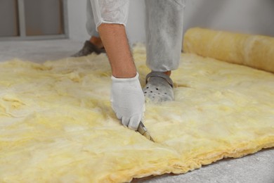 Photo of Worker in gloves cutting insulation material indoors, closeup