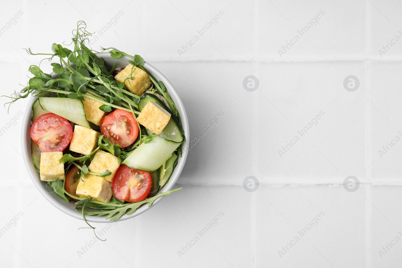 Photo of Bowl of tasty salad with tofu and vegetables on white tiled table, top view. Space for text