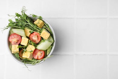 Bowl of tasty salad with tofu and vegetables on white tiled table, top view. Space for text