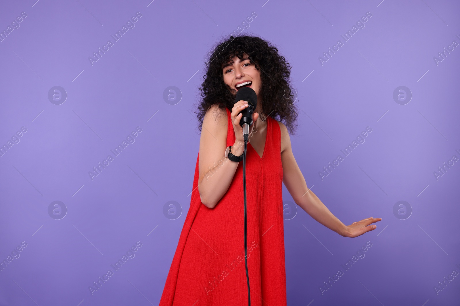 Photo of Beautiful young woman with microphone singing on purple background