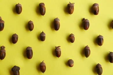 Photo of Many acorns on yellow background, flat lay