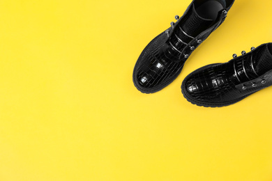 Pair of stylish ankle boots on yellow background, top view. Space for text