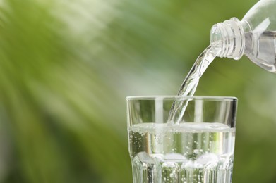 Photo of Pouring water from bottle into glass on blurred green background, closeup. Space for text