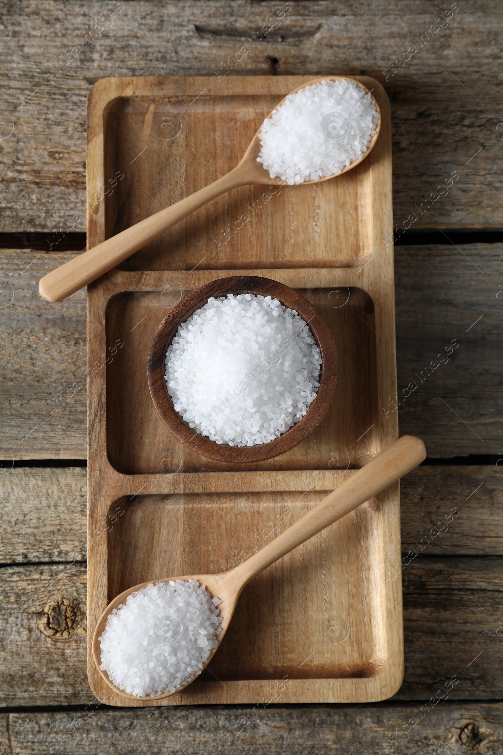 Photo of Organic salt in bowl and spoons on wooden table, top view