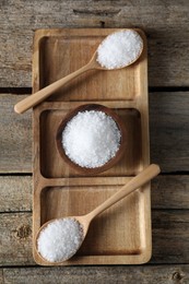 Organic salt in bowl and spoons on wooden table, top view