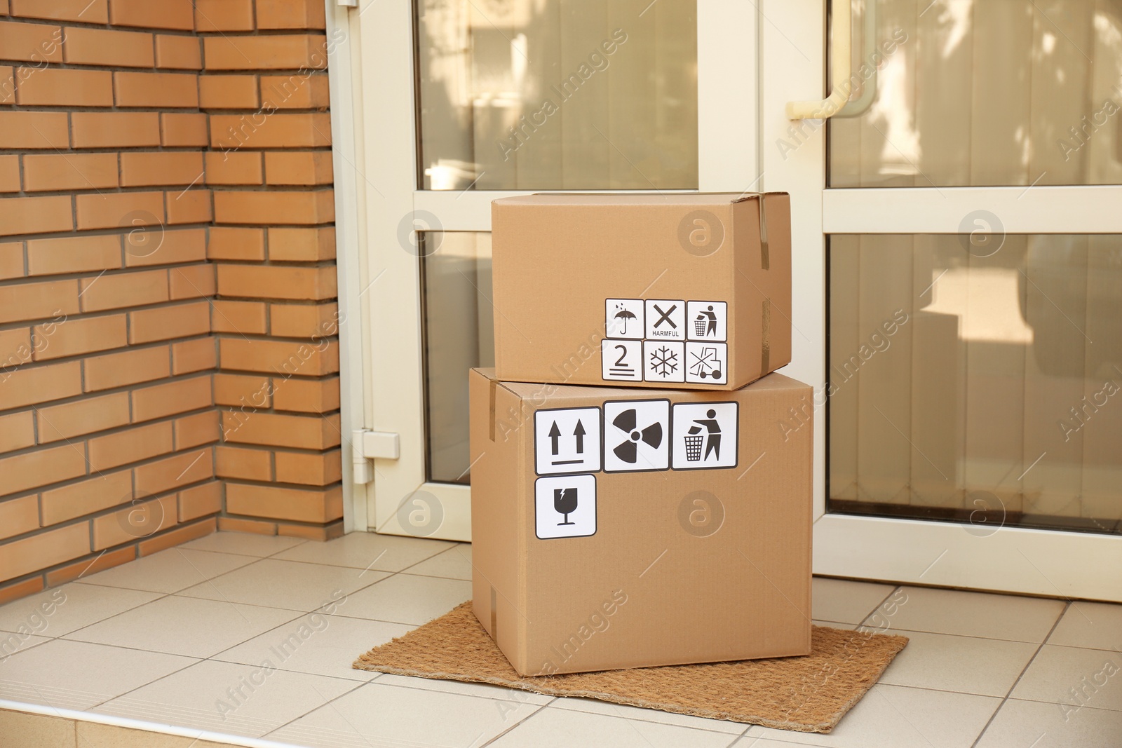 Photo of Cardboard boxes with different packaging symbols on door mat near entrance. Parcel delivery