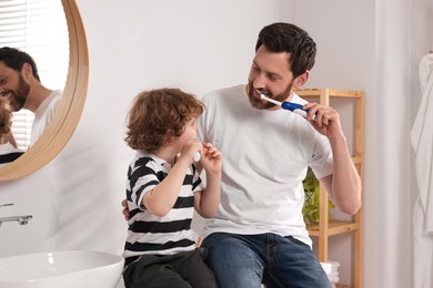 Father and his son brushing teeth together in bathroom