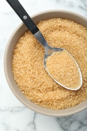 Photo of Brown sugar in bowl and spoon on white marble table, top view