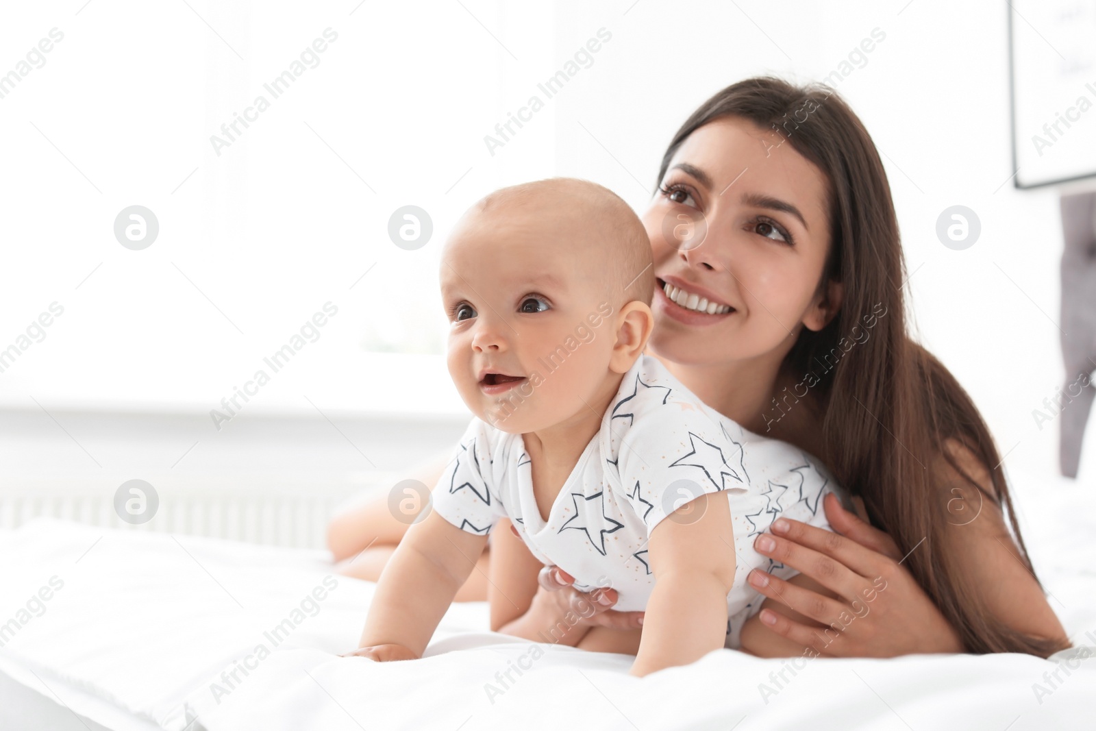 Photo of Young mother with her cute baby girl on bed at home