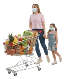 Photo of Mother and daughter in medical masks with shopping cart full of groceries on white background