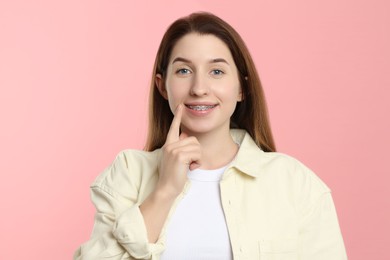 Portrait of smiling woman pointing at her dental braces on pink background