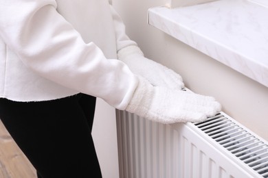 Photo of Girl warming hands on heating radiator indoors, closeup