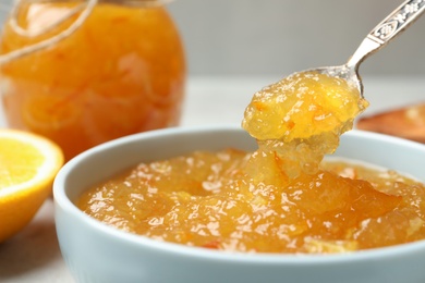 Spoon with delicious orange marmalade over bowl on table, closeup