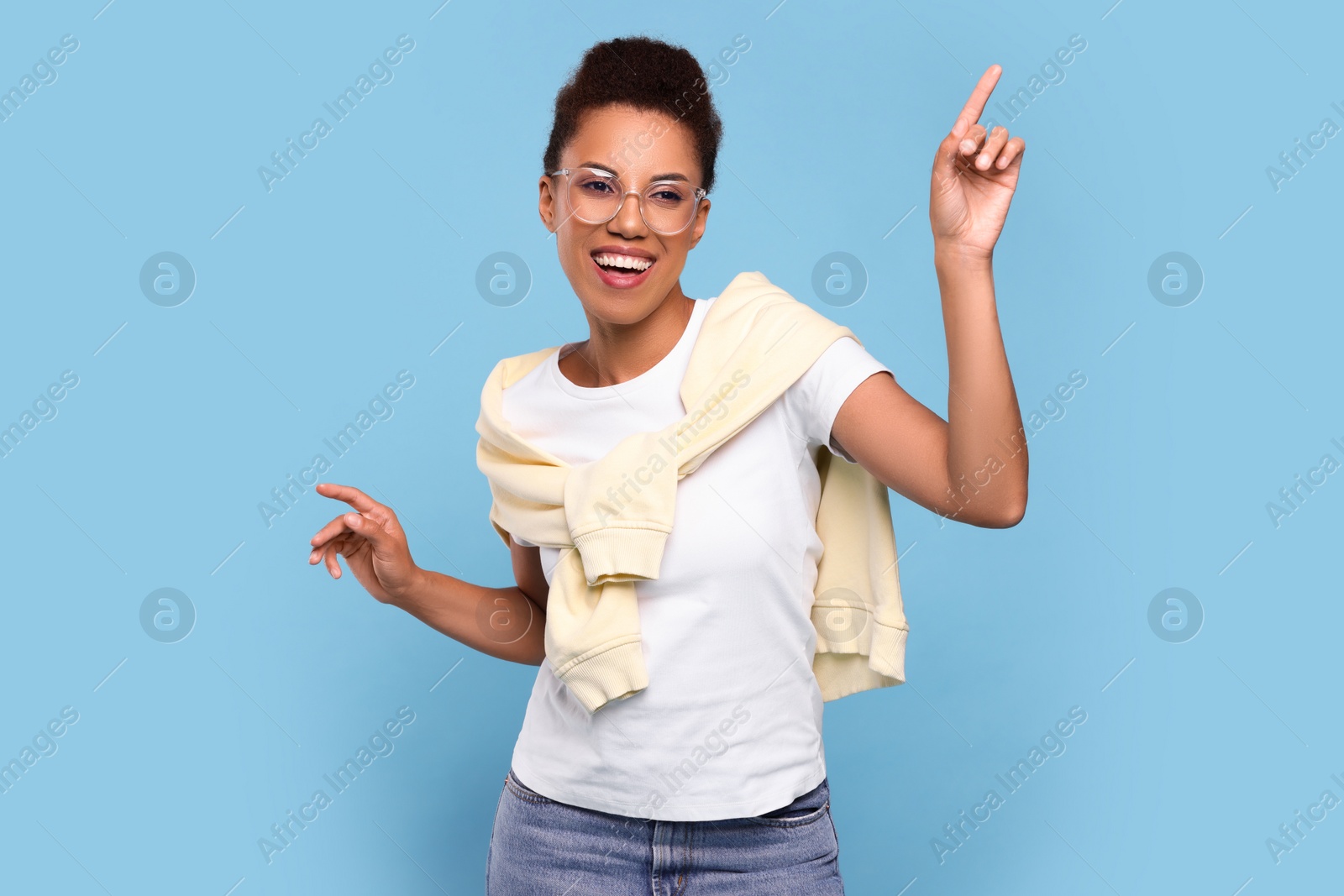 Photo of Happy young woman in stylish eyeglasses dancing on light blue background