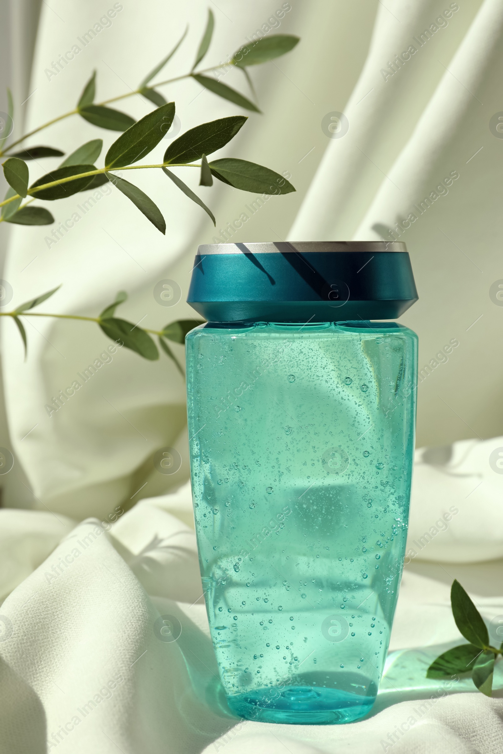 Photo of Bottle of hair care cosmetic product and green leaves on light fabric