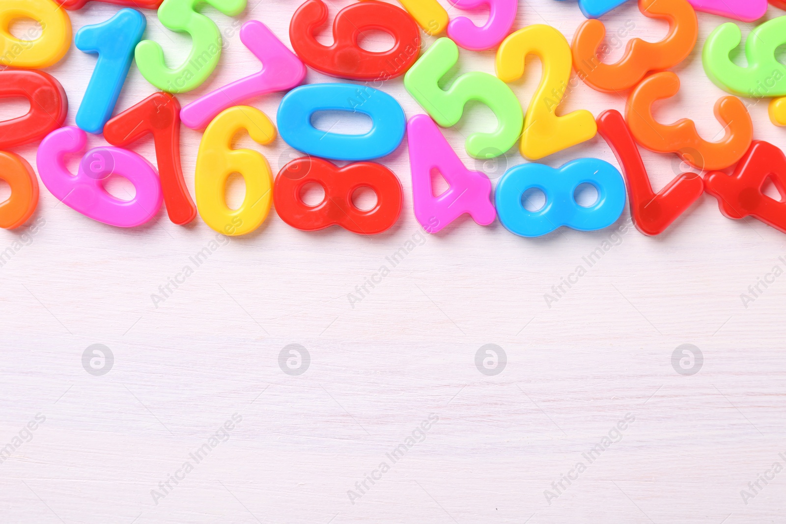 Photo of Colorful numbers on white wooden school desk, flat lay. Space for text