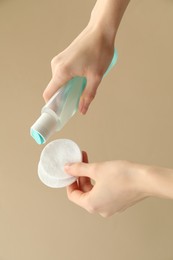 Photo of Woman pouring makeup remover onto cotton pads on beige background, closeup