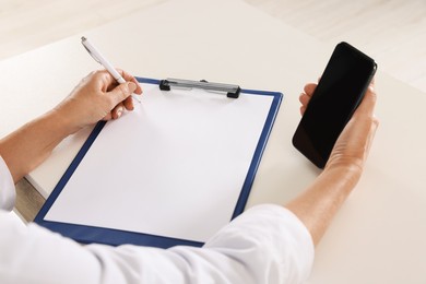 Doctor with smartphone and clipboard at desk, closeup. Online medicine concept