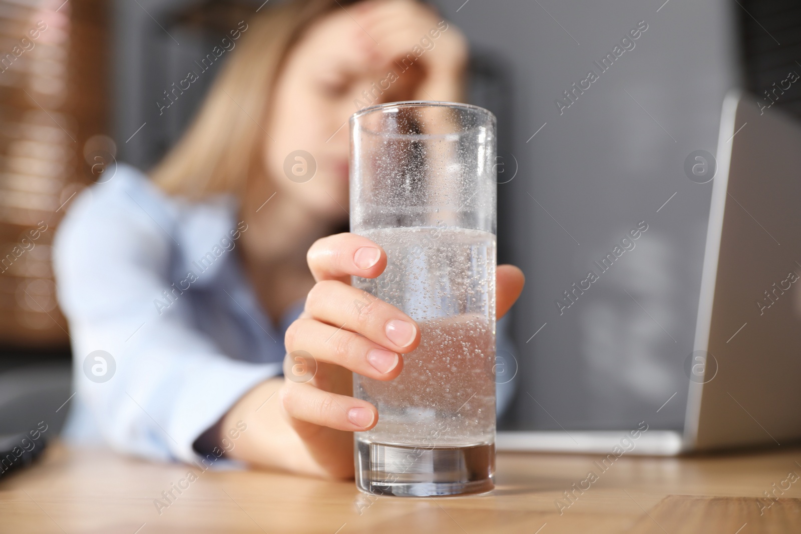 Photo of Woman taking medicine for hangover in office, focus on hand with glass