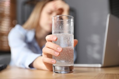 Photo of Woman taking medicine for hangover in office, focus on hand with glass