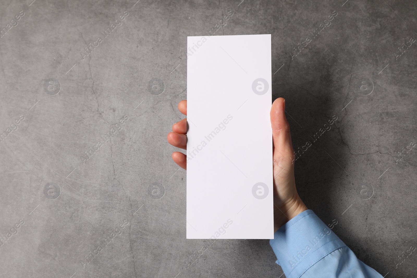 Photo of Woman holding blank card at grey table, top view. Mockup for design