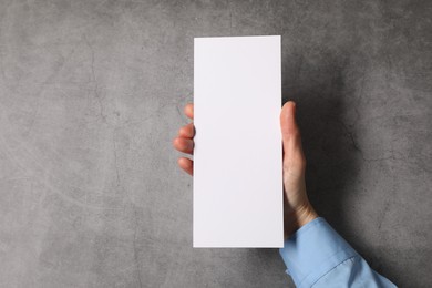 Woman holding blank card at grey table, top view. Mockup for design