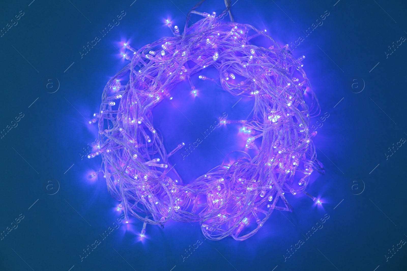 Photo of Glowing Christmas lights on dark blue background, top view