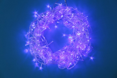 Photo of Glowing Christmas lights on dark blue background, top view