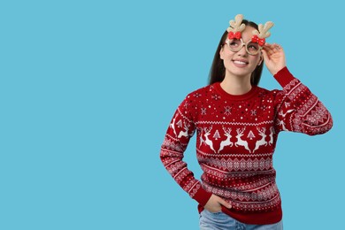 Photo of Happy young woman in Christmas sweater and funny glasses on light blue background. Space for text