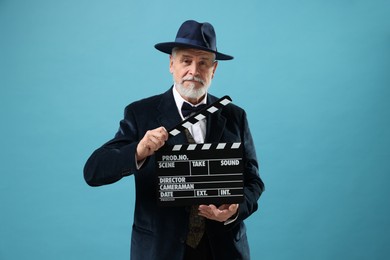 Photo of Senior actor with clapperboard on light blue background. Film industry