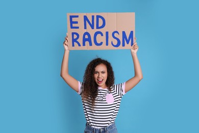 Emotional African American woman holding sign with phrase End Racism on light blue background