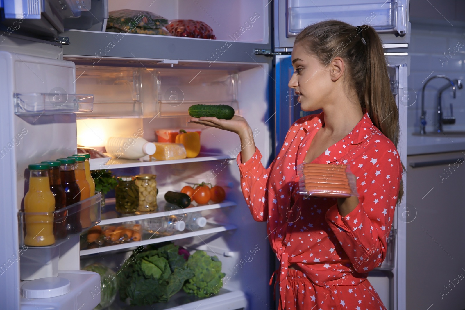 Photo of Young woman choosing food in refrigerator at night