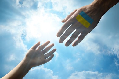 Image of Help for Ukraine. Man and child hands with drawing of Ukrainian flag and beautiful blue sky on background, closeup