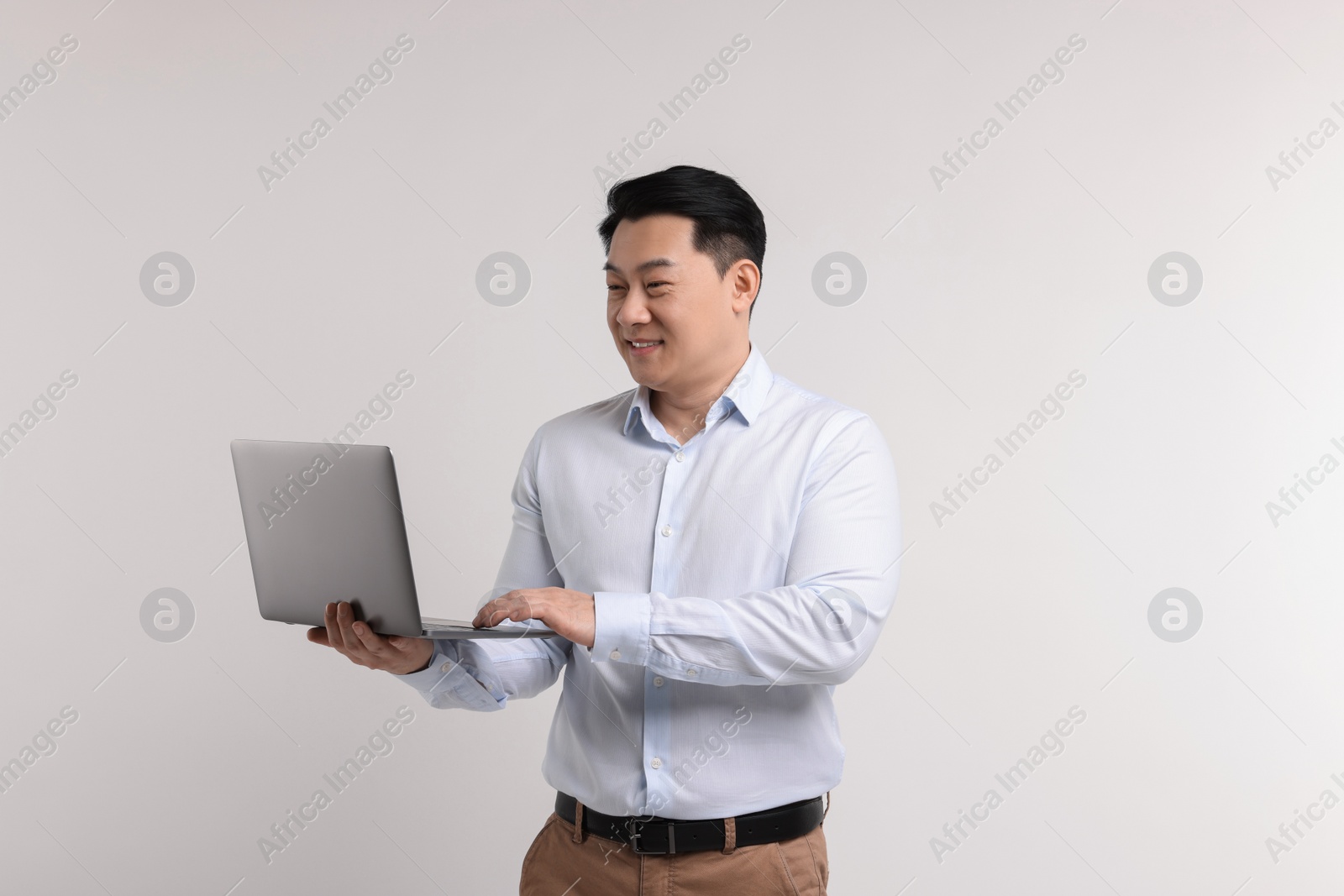 Photo of Portrait of happy man with laptop on light background
