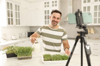 Photo of Teacher with microgreens and watering can conducting online course in kitchen. Time for hobby