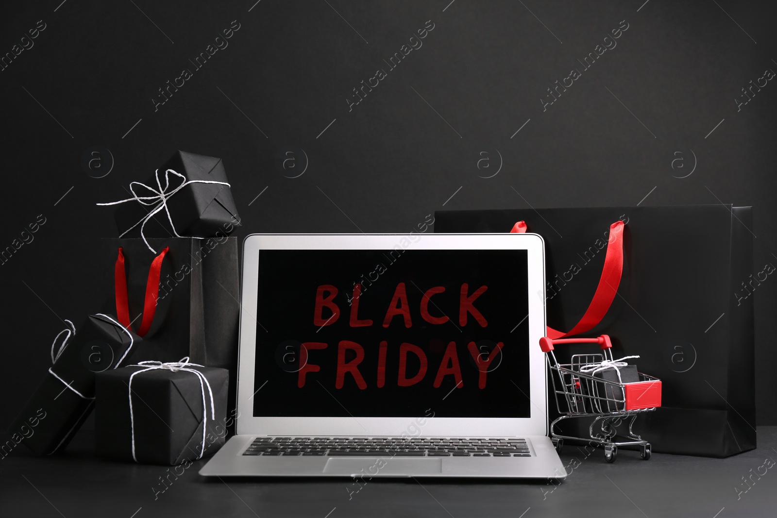 Photo of Composition with laptop and gifts on table against dark background. Black Friday sale