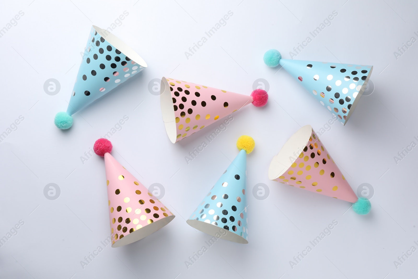 Photo of Colorful party hats with pompoms on light background, top view