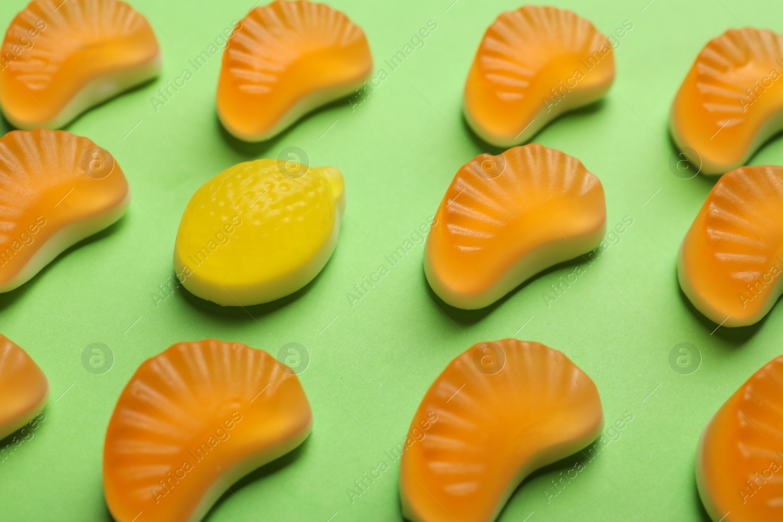 Photo of Delicious gummy orange and lemon candies on green background, closeup