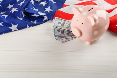 Photo of Piggy bank, American flag and dollar banknotes on white wooden table, space for text