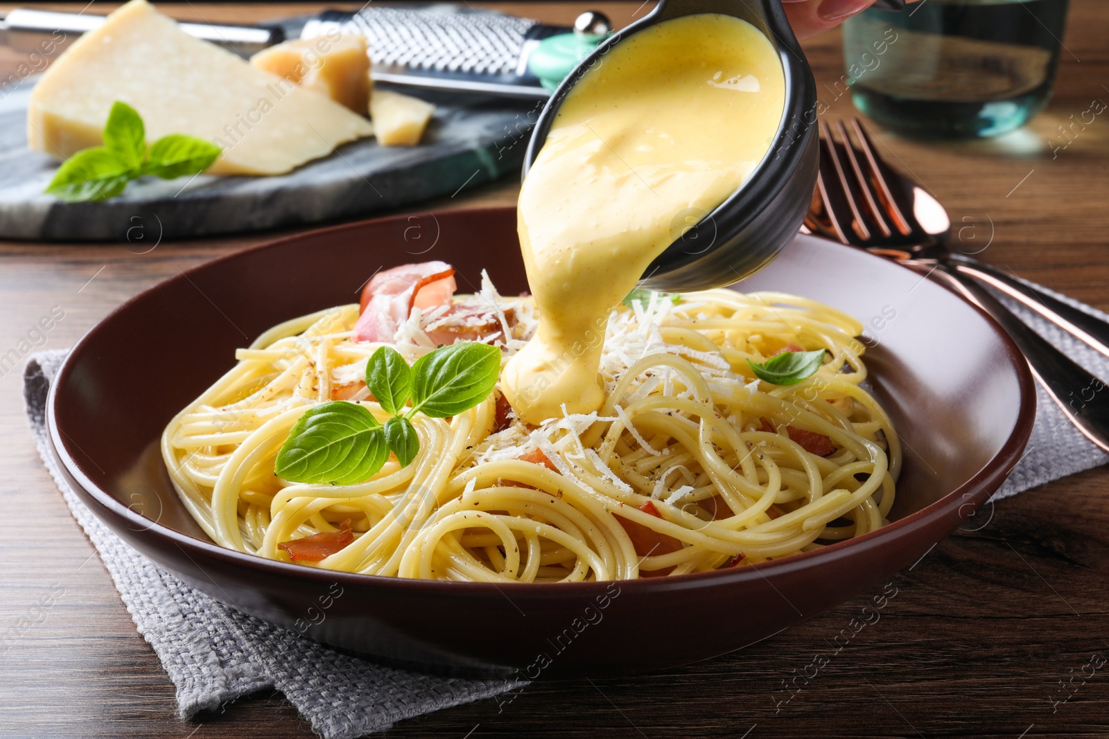 Photo of Pouring tasty cheese sauce onto spaghetti with meat on wooden table, closeup