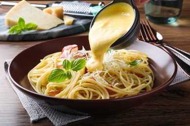 Photo of Pouring tasty cheese sauce onto spaghetti with meat on wooden table, closeup
