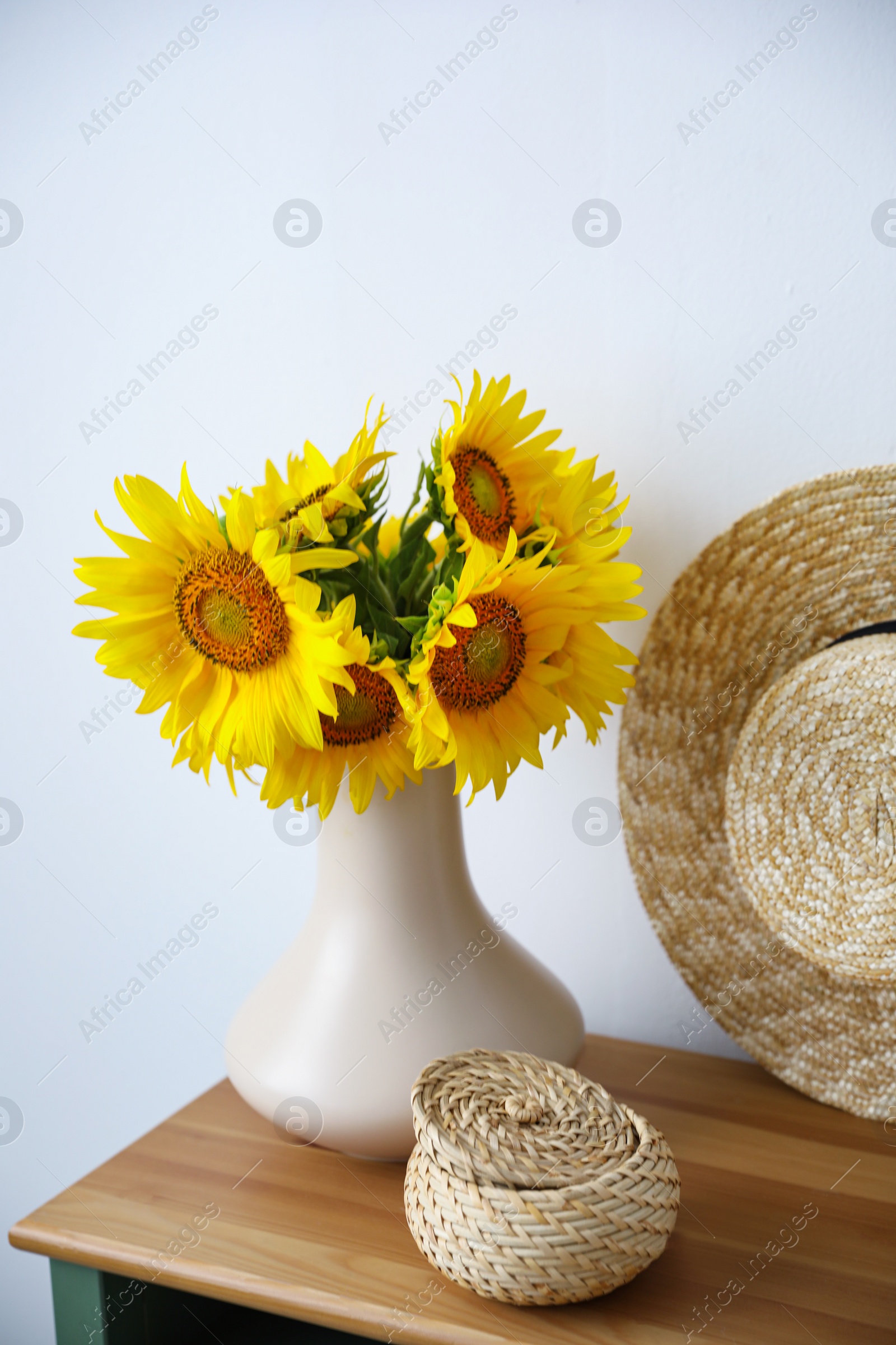 Photo of Bouquet of beautiful sunflowers, wicker basket and hat on table indoors